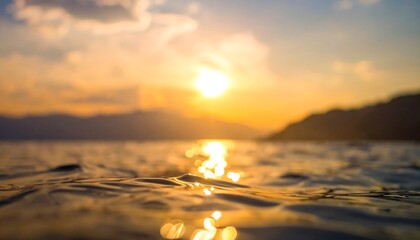 Close-up of water at sunset. Sun reflects onto water with warm orange and yellow hues, a hazy mountain range in background