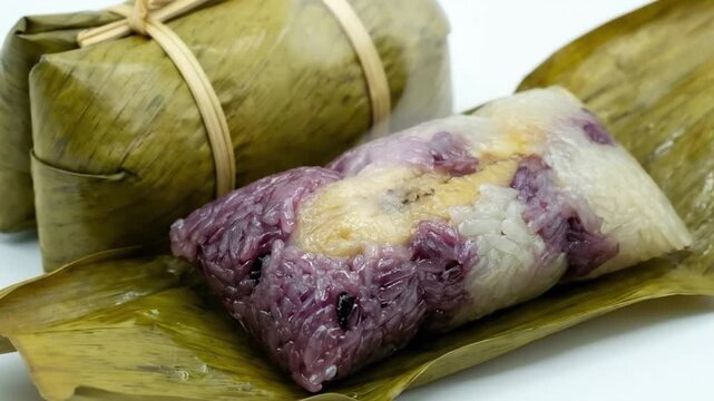 A visually appealing close-up shot captures a delicious, traditional sticky rice delicacy, meticulously wrapped in a natural leaf. One portion remains fully encased and tied with a natural fiber, whil
