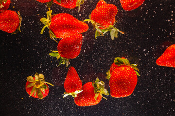 High speed capture of ripe red strawberries suspended in water with dynamic splashes against a dark background. This image conveys freshness, vitality, 