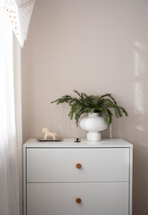 a white dresser with wooden knobs, a textured white vase with greenery, a small horse figurine, and a decorative candle holder. Soft light and a star-patterned lampshade add coziness.
