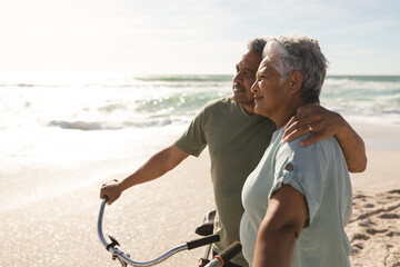 Thoughtful multiracial senior couple looking away while standing with bicycles at sunny beach © wavebreak3