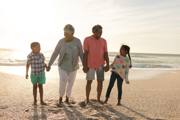 Full length of smiling senior man and woman holding hands with grandchildren at beach