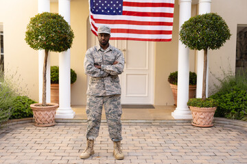 Portrait of confident african american army man in uniform with arms crossed against flag on house