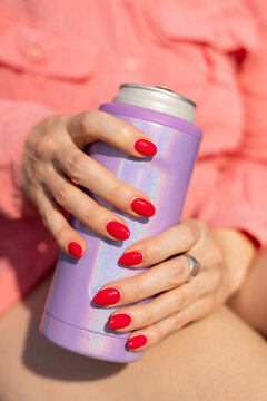 Manicured hands with red nails hold cold drink on sunny summer d