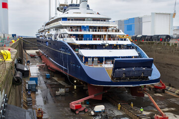 An eco-friendly cargo ship with masts for sails in a dry dock at a shipyard in Saint Nazaire, France, with cranes and construction or repair equipment