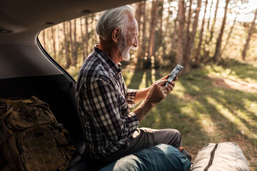 Senior man using smartphone sitting in car trunk during nature trip © Jelena