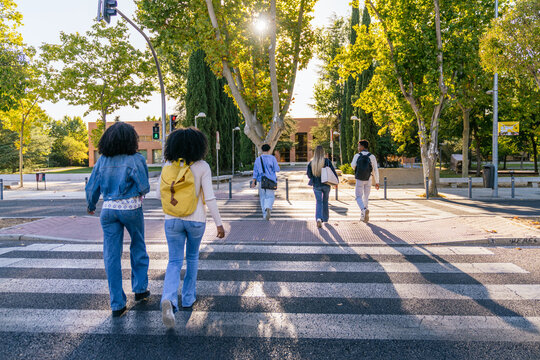 Multiracial students walking on a zebra crossing outside a university campus, showing diversity and education concept