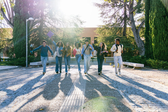 Group of excited multiracial students running together on university campus, celebrating academic success and friendship