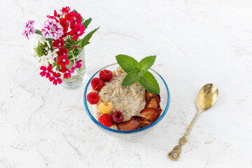 Oatmeal porridge with berries in a glass bowl on the white table.