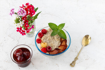 Oatmeal porridge with berries in a glass bowl on the white table.