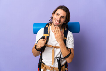 Young mountaineer man with a big backpack over isolated background looking up while smiling