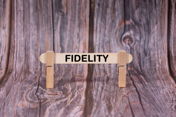 Fototapeta premium Fidelity symbol. A wooden stick clasped by clothespins set over a beautiful Brown Grunge Wooden Texture Background. Business and Fidelity concept with copy space