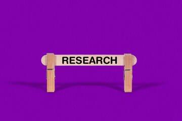 Fototapeta premium Research symbol. Wooden stick suspended by Clothespins, Purple hues Backdrop. Business and Research concept with copy space