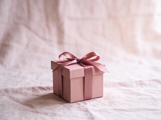 Minimal pink gift box with satin ribbon bow on soft fabric background with copy space for Valentine's Day, birthday, or anniversary celebration concept