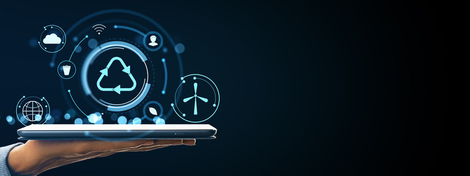 Hand holding tablet with glowing eco technology icons including recycling and wind energy symbols on dark background, symbolizing sustainability concept. - Powered by Adobe
