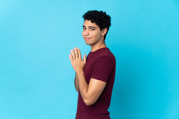 Young Venezuelan man isolated on blue background scheming something