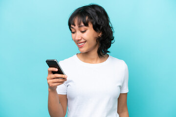 Young Argentinian woman isolated on blue background sending a message or email with the mobile