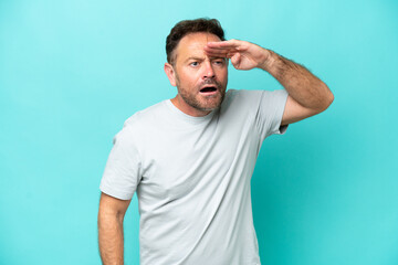 Middle age caucasian man isolated on blue background looking far away with hand to look something