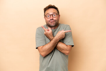 Middle age caucasian man isolated on beige background pointing to the laterals having doubts