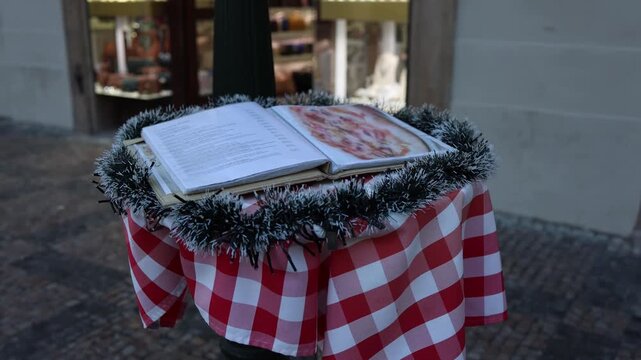 Restaurant menu displayed on outdoor stand decorated with christmas garland inviting passersby to choose meals in festive street cafe atmosphere