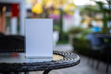 Copy space menu mockup concept with a blank white tabletop sign on a restaurant table, blurred cafe background and warm lights, perfect for advertising, branding, and food specials.