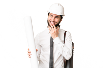 Young architect man with helmet and holding blueprints over isolated chroma key background looking up while smiling