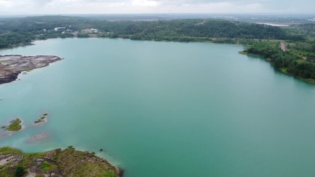A hole from a coal mine that holds blue water and shows the remains of trees that have been cut down