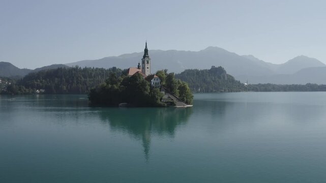 4K aerial drone shot rising and flying towards Lake Bled island with the church, castle and Julian Alps in background