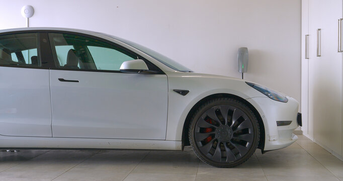 CLOSE UP: Scratched Tesla car connected to a charging station in home garage