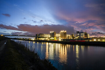The Gersthofen industrial park, a chemical and industrial site with futuristic-looking buildings and silo facilities. The green bridge construction spans the Lech Canal. Colorful cloudy evening sky