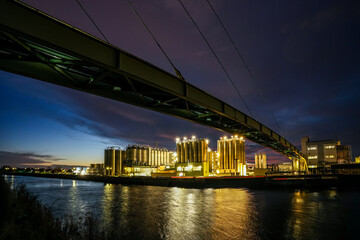 The Gersthofen industrial park, a chemical and industrial site with futuristic-looking buildings and silo facilities. The green bridge construction spans the Lech Canal. Colorful cloudy evening sky