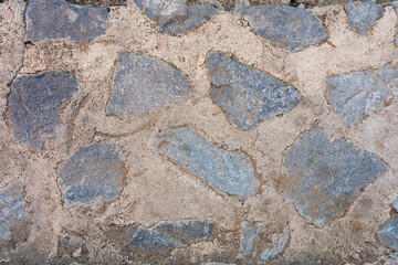 Close up of a weathered stone wall surface with irregular blue gray rocks set in light brown mortar