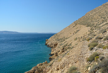 Narrow rocky hiking path along the steep cliffs on the western coast of Vela Draga in the southern part of Krk island overlooking the blue Adriatic sea