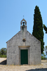 Front view of the traditional stone chapel of Saint Roch in Karmen near Orebic showing the bell tower and green doors against a clear blue sky