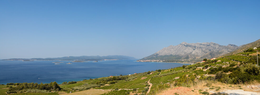 A wide panoramic view from the Peljesac peninsula showing the island of Korcula on the left and the coastal town of Orebic at the foot of the mountains on the right