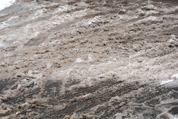 A close up of grey melting slush and dirty snow on a city street with visible tire tracks and messy texture during winter thaw.