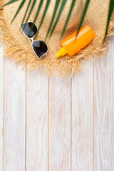 Vacation travel planning simple background of straw hat sunglasses palm leaves and sunblock lotion on white planks flat lay with copy-space