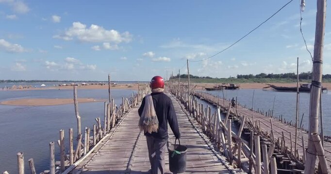 Fisherman with a net and bucket walks across the Koh Paen bamboo bridge in Kampong Cham