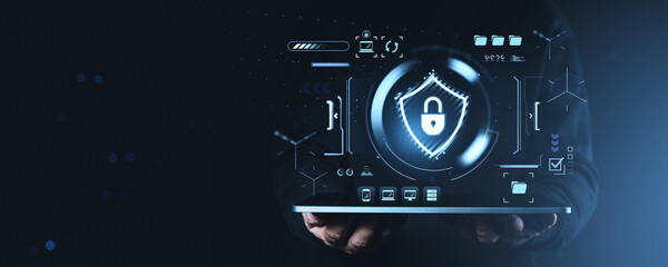 Cybersecurity shield and lock icon on futuristic interface above tablet held by person in dark hoodie, symbolizing data protection and privacy concept.