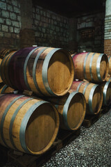 Rows of traditional oak wine barrels aging in a dim, authentic stone cellar of a historic winery