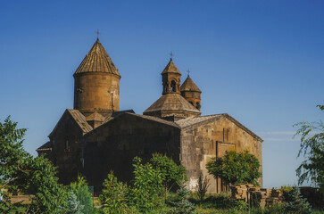Ancient Armenian stone monastery Saghmosavank with traditional conical domes under a clear blue sky surrounded by green trees