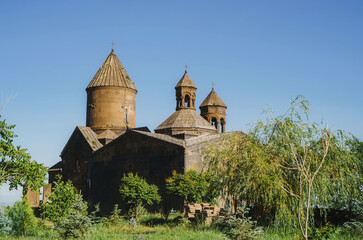 Ancient Armenian stone monastery Saghmosavank with traditional conical domes under a clear blue sky surrounded by green trees