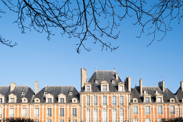 Typical facade of the historic buildings surrounding the Place des Vosges in Paris with bare tree branches above