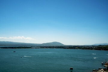 Wide panoramic view of Lake Sevan with turquoise water, small boats, and green mountain shores under a clear blue sky