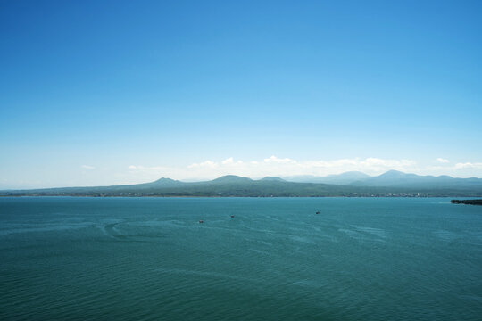 Wide panoramic view of Lake Sevan with turquoise water, small boats, and green mountain shores under a clear blue sky