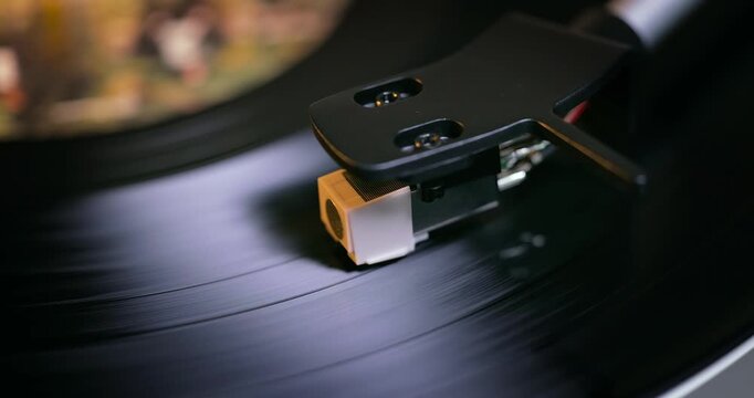 Detailed close-up of a turntable tonearm with white cartridge headshell, positioned over a black vinyl record on the platter, highlighting audio equipment precision.