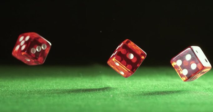 Red dice falling and bouncing on green table on a dark background. Shot on super slow motion camera 1000 fps.