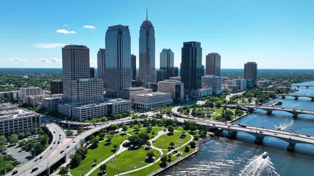 A city skyline of tall glass towers beside a winding river, green park, and bridges with riverfront