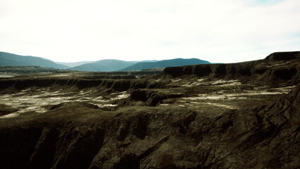 Vast, rugged formations stretch across the landscape, with shadows cast by distant mountain peaks under a soft, cloudy sky. Earth tones dominate the ground, revealing natures raw beauty.