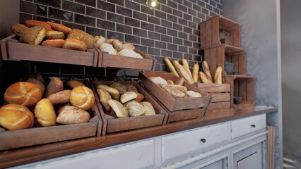 Warm rolls, crusty baguettes, and artisanal loaves are creatively arranged on rustic wooden shelves in a cozy bakery. Soft lighting adds to the inviting atmosphere.
